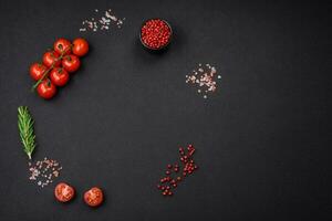 Empty black texture table, cherry tomatoes on a twig, spices, salt and herbs photo