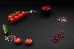 Empty black texture table, cherry tomatoes on a twig, spices, salt and herbs photo