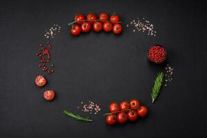 Empty black texture table, cherry tomatoes on a twig, spices, salt and herbs photo