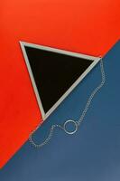 top view of triangle mirror in silver frame on a color blue and red background. Creative backdrop photo