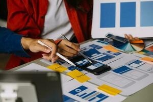 Close up ux developer and ui designer brainstorming about mobile app interface wireframe design on table with customer breif and color code at modern office.Creative digital development agency photo