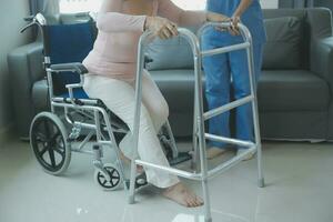 Asian young woman nurse at nursing home take care disabled senior man. Caregiver doctor serve physical therapy for older elderly patient to exercise and practice walking on walker or cane at backyard. photo