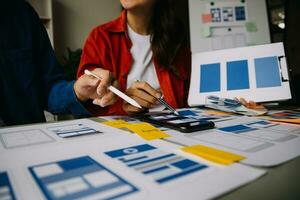 Close up ux developer and ui designer brainstorming about mobile app interface wireframe design on table with customer breif and color code at modern office.Creative digital development agency photo