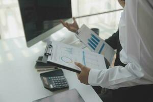 Group of confident business people point to graphs and charts to analyze market data, balance sheet, account, net profit to plan new sales strategies to increase production capacity. photo