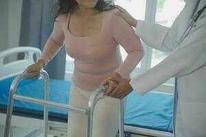 young asian physical therapist working with senior woman on walking with a walker photo