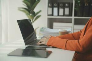 atractivo sonriente joven asiático negocio mujer trabajo a hogar oficina, asiático mujer trabajando en ordenador portátil computadora participación tableta. foto