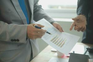 Group of confident business people point to graphs and charts to analyze market data, balance sheet, account, net profit to plan new sales strategies to increase production capacity. photo