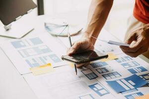 Close up ux developer and ui designer brainstorming about mobile app interface wireframe design on table with customer breif and color code at modern office.Creative digital development agency photo