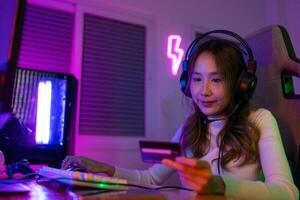 Top up online game with credit card concept. Gamer and E-Sport online of Asian woman playing online computer video game with lighting effect, broadcast streaming live at home. Gamer and E-Sport gaming photo