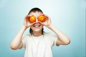 happy smiling boy with two mandarins covering his eyes on blue background. photo