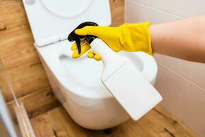 Close-up of gloved hands using toilet bowl sanitizer solution, bottle mockup photo