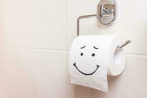 close-up, a roll of toilet paper with a painted sad face stands on the toilet photo