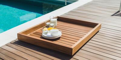 A wooden tray on a wooden deck next to swimming pool photo