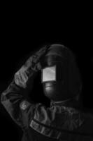 soldador hombre en el casco y con soldadura terminales en el mano en el negro pared antecedentes con Copiar espacio muestra un pulgares arriba gesto. foto