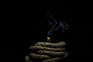 extinguished wax candle with a wick old shabby book twisted rope on a black background photo
