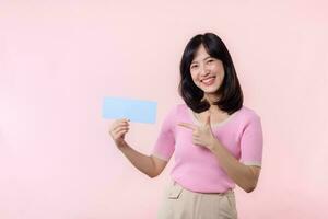 Portrait happy young woman model holding and showing blank space paper for advertisement information message poster with thumb up or point finger gesture isolated on pink pastel studio background. photo