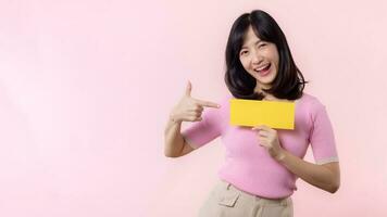 Portrait happy young woman model holding and showing blank space paper for advertisement information message poster with thumb up or point finger gesture isolated on pink pastel studio background. photo