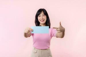 Portrait happy young woman model holding and showing blank space paper for advertisement information message poster with thumb up or point finger gesture isolated on pink pastel studio background. photo