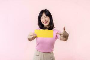 Portrait happy young woman model holding and showing blank space paper for advertisement information message poster with thumb up or point finger gesture isolated on pink pastel studio background. photo