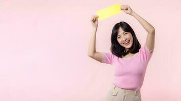 Portrait happy young woman model holding and showing blank space paper for advertisement information message poster with thumb up or point finger gesture isolated on pink pastel studio background. photo