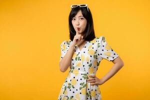 Portrait young asian woman hushing with index finger shares secret makes taboo gesture sign wears casual springtime dress isolated on yellow background. Shh be quiet concept photo