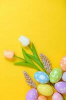 Happy Easter holiday greeting card design concept. Colorful Easter Eggs and spring flowers on yellow background. Flat lay, top view, copy space. photo