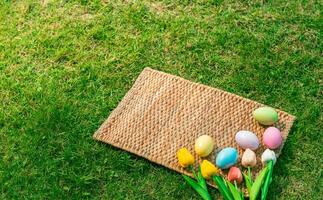 Happy Easter holiday greeting card concept. Colorful Easter Eggs and spring flowers on Papyrus rattan weave texture background. Flat lay, top view, copy space. photo