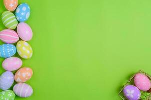 Happy Easter holiday greeting card design concept. Colorful Easter Eggs and spring flowers on pastel green background. Flat lay, top view, copy space. photo