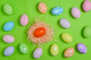 Happy Easter holiday greeting card design concept. Colorful Easter Eggs and spring flowers on pastel green background. Flat lay, top view, copy space. photo