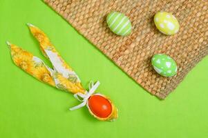 Happy Easter holiday greeting card design concept. Colorful Easter Eggs and spring flowers on pastel green background. Flat lay, top view, copy space. photo