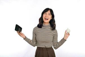 Portrait of young Asian woman casual uniform holding white piggy bank and calculator isolated on white background, Financial and bank saving money concept photo