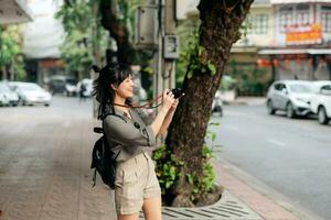 Young Asian woman backpack traveler using digital compact camera, enjoying street cultural local place and smile. Traveler checking out side streets. photo