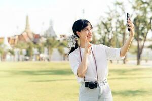 Portrait beautiful young asian woman with smartphone on summer holiday vacation trip with the grand palace in a background at Bangkok, Thailand photo