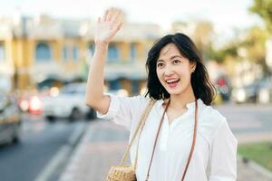 Portrait young beautiful asian woman waving hand to friend by the street in sunny holiday. photo