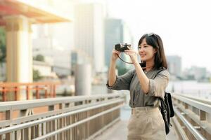 Young Asian woman backpack traveler using a camera in express boat pier on Chao Phraya River in Bangkok. photo