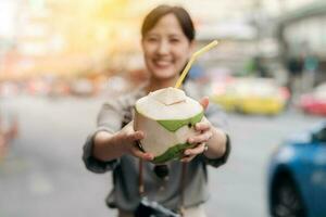 contento joven asiático mujer mochila viajero Bebiendo un Coco jugo a China pueblo calle comida mercado en bangkok, tailandia viajero comprobación fuera lado calles foto