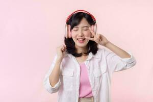 Smile pretty asian model person listen music song and enjoy dance with wireless headphone online audio radio sound. Positive fun exited joyful youth female woman on pink isolated background studio photo