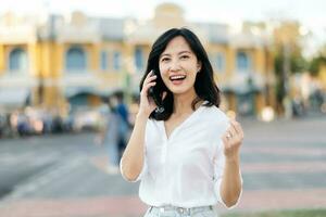 Portrait beautiful young asian woman receiving good news on mobile phone and arms raised feeling cheerful ,happiness. around outdoor street view in a summer day photo