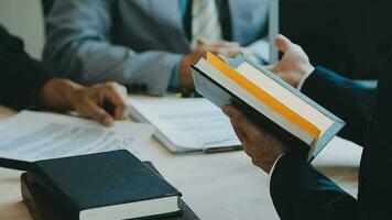 Business and lawyers discussing contract papers with brass scale on desk in office. Law, legal services, advice, justice and law concept picture with film grain effect video