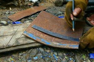 a hand is using a pencil and a ruler to measure the rusted iron to be cut photo