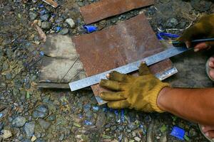 a hand is using a pencil and a ruler to measure the rusted iron to be cut photo