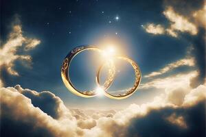 A pair of gold wedding rings floating in the sky. two wedding rings floating in the clouds with a sun in the background and a blue sky with clouds below them. . Wedding concept. photo