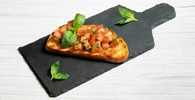 bruschetta on a black plate, on a white wooden background photo