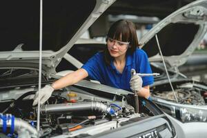 hembra mecánico trabajando en un coche servicio. un mujer vistiendo guantes y utilizando un rueda debajo un taller coche. reparar Servicio concepto coche reparar y mantenimiento. foto