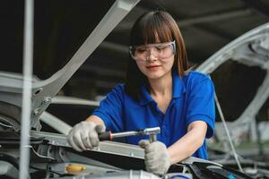 contento asiático mujer auto mecánico en cochera. profesional auto mecánico quien inspecciona y refacción motor en cochera. coche reparar y mantenimiento concepto. foto