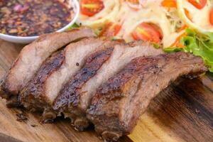 bistec de cerdo asado en el plato de madera con salsa tailandesa. foto