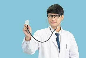 asiático hombre estudiante científico o médico uno persona, vistiendo un blanco vestido, de pie, mirando y sonriente, azul antecedentes con un estetoscopio auscultando el corazón alrededor su cuello. foto