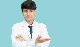 asiático hombre estudiante científico o médico uno persona, vistiendo un blanco vestido, de pie, mirando y sonriente, azul antecedentes con un estetoscopio auscultando el corazón alrededor su cuello. foto