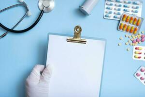 Blank tablet mockup in gloved hand with colorful pills and stethoscope. Healthcare and medicine concept flat lay photo