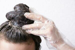 Women's hair is collected in a bun with paint applied to it and gloved hand. Hair dyeing concept photo